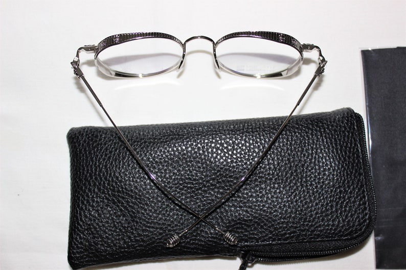 May include: Silver-toned round eyeglasses with a black leather case and a black microfiber cleaning cloth.
