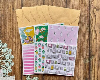 Pode incluir: Um conjunto de seis cartões de papel com padrões com vários desenhos, incluindo padrões florais, de coelhos e de janelas. Os cartões estão dispostos em uma pilha e todos são em tons de rosa, verde e amarelo.