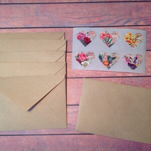 Peut inclure: Une pile de six enveloppes en papier kraft brun avec une seule enveloppe brune &agrave; droite. Les enveloppes sont toutes ferm&eacute;es et ont un autocollant en forme de c&oelig;ur blanc avec des motifs floraux.