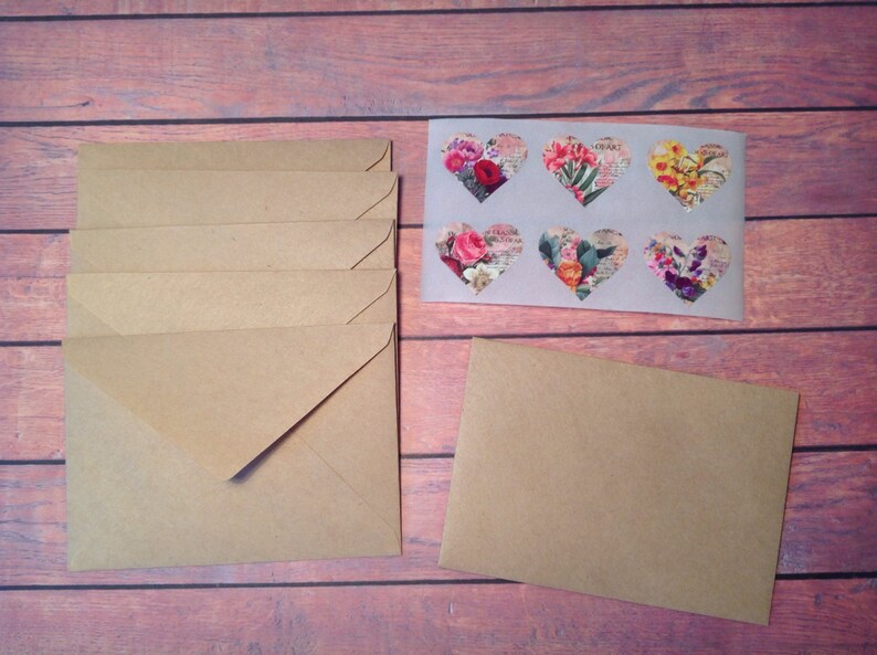 Peut inclure: Une pile de six enveloppes en papier kraft brun avec une seule enveloppe brune &agrave; droite. Les enveloppes sont toutes ferm&eacute;es et ont un autocollant en forme de c&oelig;ur blanc avec des motifs floraux.