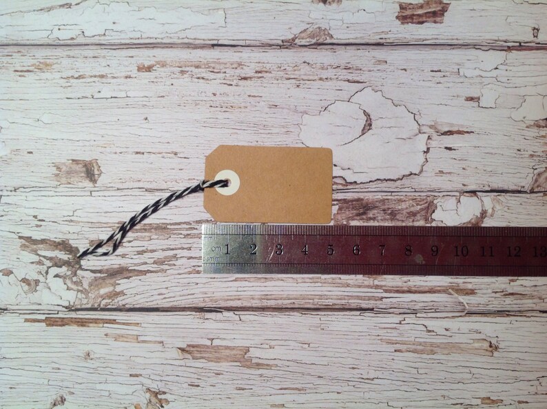 May include: A brown paper gift tag with a white circle and a black and white string attached. The tag is lying on a white wooden surface with a ruler next to it.