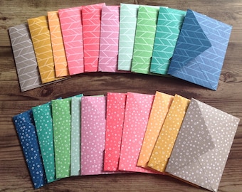 May include: A set of 20 colourful patterned envelopes with geometric and polka dot designs. The envelopes are arranged in two semi-circles.