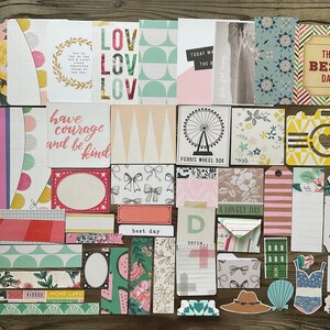 May include: A collection of colorful paper craft supplies with various designs and patterns. The papers feature text such as "have courage and be kind", "the best day", and "a lovely day".