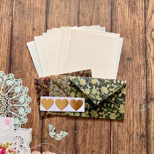 Peut inclure: Un ensemble de papeterie vierge avec des enveloppes. Les enveloppes sont décorées de motifs floraux dans des tons de brun, vert et jaune. Il y a trois autocollants en forme de cœur dorés sur le papier blanc.