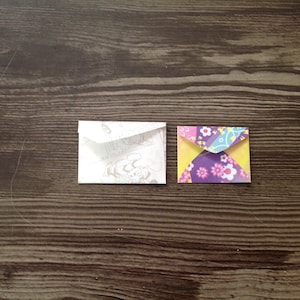 May include: Two small envelopes, one white with a patterned design and one with a colorful floral pattern.