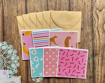 Pode incluir: Conjunto de seis cartões de felicitação em branco com padrões diferentes. Os padrões incluem listras rosa e brancas, rosa com corações brancos, rosa com rabiscos vermelhos, rosa com bananas amarelas, rosa com margaridas brancas e rosa com leopardos laranja.