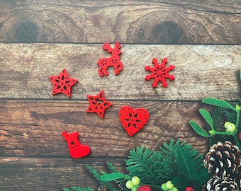 May include: Red wooden Christmas ornaments in various shapes, including stars, a reindeer, a snowflake, a heart, and a stocking. The ornaments are arranged on a wooden surface with greenery and pine cones.