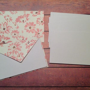 Puede incluir: Un juego de tarjetas en blanco con sobres. Los sobres tienen un patr&oacute;n floral con flores rosas sobre un fondo crema.