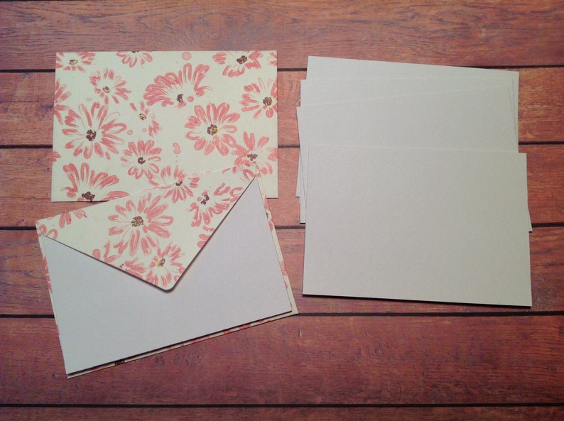 Puede incluir: Un juego de tarjetas en blanco con sobres. Los sobres tienen un patr&oacute;n floral con flores rosas sobre un fondo crema.