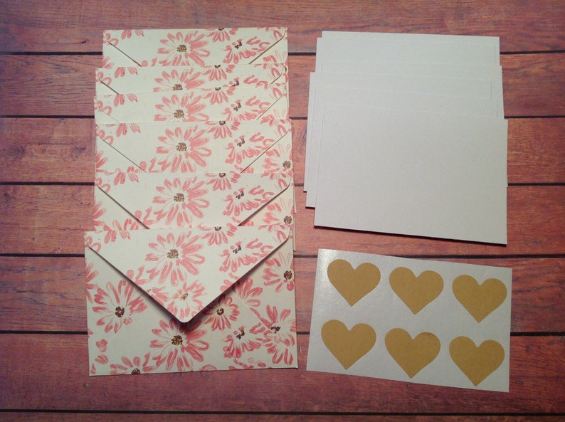 Puede incluir: Un juego de ocho sobres blancos con un patr&oacute;n floral rosa, una pila de tarjetas blancas y una hoja de seis pegatinas doradas en forma de coraz&oacute;n.