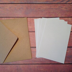 Peut inclure: Une enveloppe en papier brun et une pile de papier cartonn&eacute; blanc sur une surface en bois.