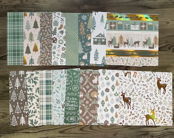 May include: A collection of Christmas-themed scrapbook paper sheets. The designs include plaid, trees, cabins, deer, and holiday greetings in shades of green, brown, and gold. The sheets are arranged in two stacks, showcasing various patterns.