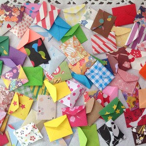 May include: A collection of colorful, patterned paper envelopes. The envelopes are small and are made of different materials, including paper, fabric, and plastic. They are arranged in a random pattern on a white surface.