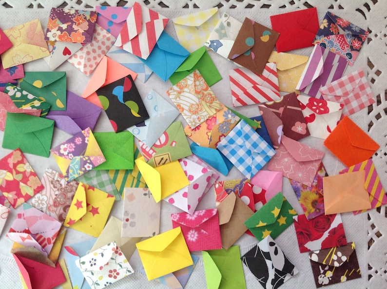 May include: A collection of colorful, patterned paper envelopes. The envelopes are small and are made of different materials, including paper, fabric, and plastic. They are arranged in a random pattern on a white surface.