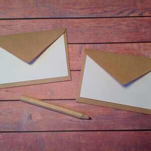 Peut inclure: Deux enveloppes brunes avec des int&eacute;rieurs blancs sont pos&eacute;es sur une surface en bois. Un crayon en bois est pos&eacute; &agrave; c&ocirc;t&eacute; des enveloppes.