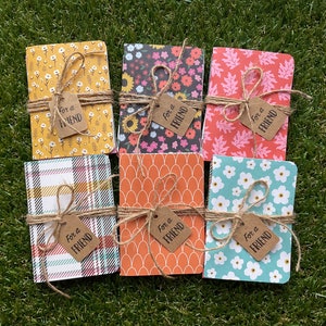 May include: Six small notebooks with different patterned covers. Each notebook is tied with twine and has a brown tag that says "For a Friend".