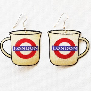May include: A pair of cream-coloured ceramic earrings shaped like mugs with a red and blue London Underground logo and the word "LONDON" printed on them.