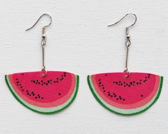 May include: A pair of watermelon slice earrings with silver hooks. The earrings are made of fabric and feature a pink watermelon slice with black seeds and a green rind.