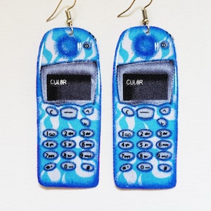 Puede incluir: Un par de pendientes de teléfono móvil azul con un diseño estampado blanco y azul. Los pendientes tienen un gancho plateado y el texto "CULBR" en la pantalla.