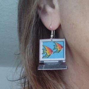 Pode incluir: Um par de brincos pendentes com uma tela de laptop com dois peixes laranja e amarelos nadando dentro. O laptop &eacute; prateado com um teclado preto.