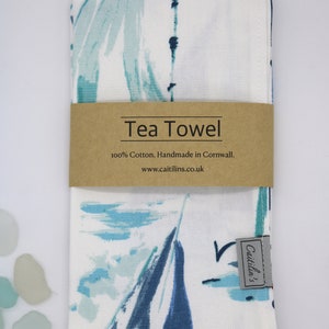 Pode incluir: Uma toalha de ch&aacute; branca com um design abstrato azul e verde. A toalha tem um r&oacute;tulo castanho que diz "Tea Towel 100% Cotton. Handmade in Cornwall. www.caitlins.co.uk" e um r&oacute;tulo cinzento mais pequeno que diz "Caitlin's".