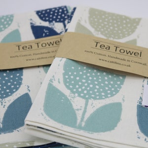Pode incluir: Duas toalhas de ch&aacute; com um design floral. As toalhas est&atilde;o dobradas e empilhadas uma em cima da outra. A toalha superior &eacute; turquesa com bolinhas brancas e a toalha inferior &eacute; azul com bolinhas brancas. As toalhas s&atilde;o etiquetadas com "Tea Towel" e "100% Algod&atilde;o. Feito &agrave; m&atilde;o na Cornualha. www.caitilins.co.uk".