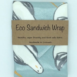 May include: A blue and white fabric sandwich wrap with a brown label that reads "Eco Sandwich Wrap" and "Reusable, vegan friendly and food safe fabric. Handmade in Cornwall."