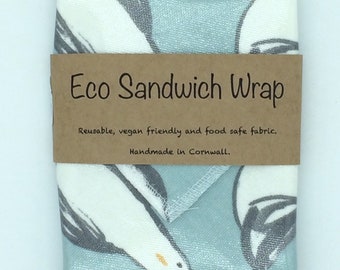 May include: A blue and white fabric sandwich wrap with a brown label that reads "Eco Sandwich Wrap" and "Reusable, vegan friendly and food safe fabric. Handmade in Cornwall."