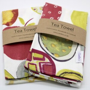Pode incluir: Duas toalhas de ch&aacute; dobradas com um design abstrato de frutas coloridas. As toalhas s&atilde;o brancas com ilustra&ccedil;&otilde;es de frutas vermelhas, amarelas e verdes. As toalhas s&atilde;o etiquetadas com "Tea Towel" e o texto "100% Algod&atilde;o, Feito &agrave; m&atilde;o na Cornualha, www.cottonandco.co.uk".
