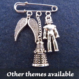 Könnte beinhalten: Silbernes Charm-Armband mit einem Sicherheitsnadelverschluss. Die Charms beinhalten einen Dalek, Engelsflügel und einen Roboter.