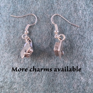 May include: A pair of silver earrings with graduation cap charms. The earrings are on a textured gray surface. More charms available.