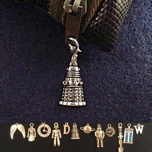May include: A silver charm of a Dalek from the Doctor Who television series. The charm is attached to a zipper pull. The charm is surrounded by other charms, including a TARDIS, a sonic screwdriver, and a fez.