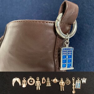 Peut inclure: Un charme argenté avec un design TARDIS en émail bleu et blanc, suspendu à un sac en cuir marron. Le charme fait partie d'un ensemble de charmes, comprenant un ange ailé, une horloge, un robot, un Dalek, une planète, un astronaute, une fleur, un tournevis sonique, un TARDIS et une lettre W.