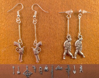 May include: Silver dangle earrings with a choice of charms: a gun, a zombie, or an arrow. The earrings are on a brown background.