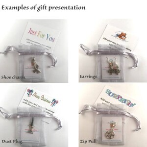May include: Four examples of gift presentation ideas. Each image shows a small gift in a white organza bag with a card. The cards have different designs and text, including "Just For You", "Merry Christmas", "Surprise!" and a teddy bear. The gifts are a shoe charm, earrings, a dust plug, and a zip pull.