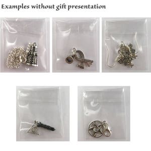 May include: Five silver charm pendants in individual clear plastic bags. The charms include a silver TARDIS, a silver infinity symbol with a silver bead, a silver charm with a detailed design, a silver charm with a triangle and a black wand, and a silver pentagram charm.