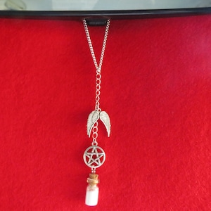 May include: A silver charm necklace with a pentagram charm, a pair of angel wings, and a small glass bottle filled with white crystals. The necklace is hanging from a rearview mirror.