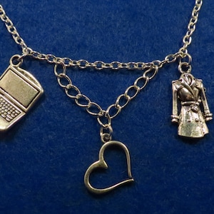 May include: Silver-toned necklace with three charms: a laptop, a heart, and a coat. The laptop charm has a detailed keyboard design. The heart charm is a simple outline. The coat charm is a miniature trench coat.