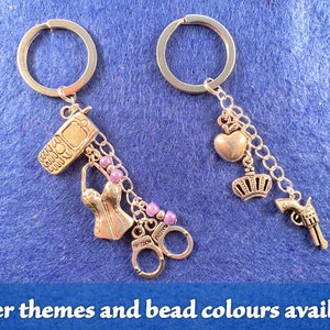 May include: Two silver keychains with charms. One keychain has a phone, a corset, handcuffs, and purple beads. The other keychain has a heart, a crown, and a gun.