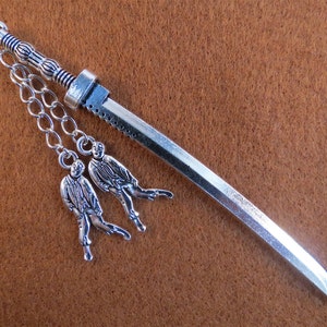 May include: Silver bookmark shaped like a sword with two small silver figures hanging from a chain. The figures are dressed in suits and have their arms outstretched.