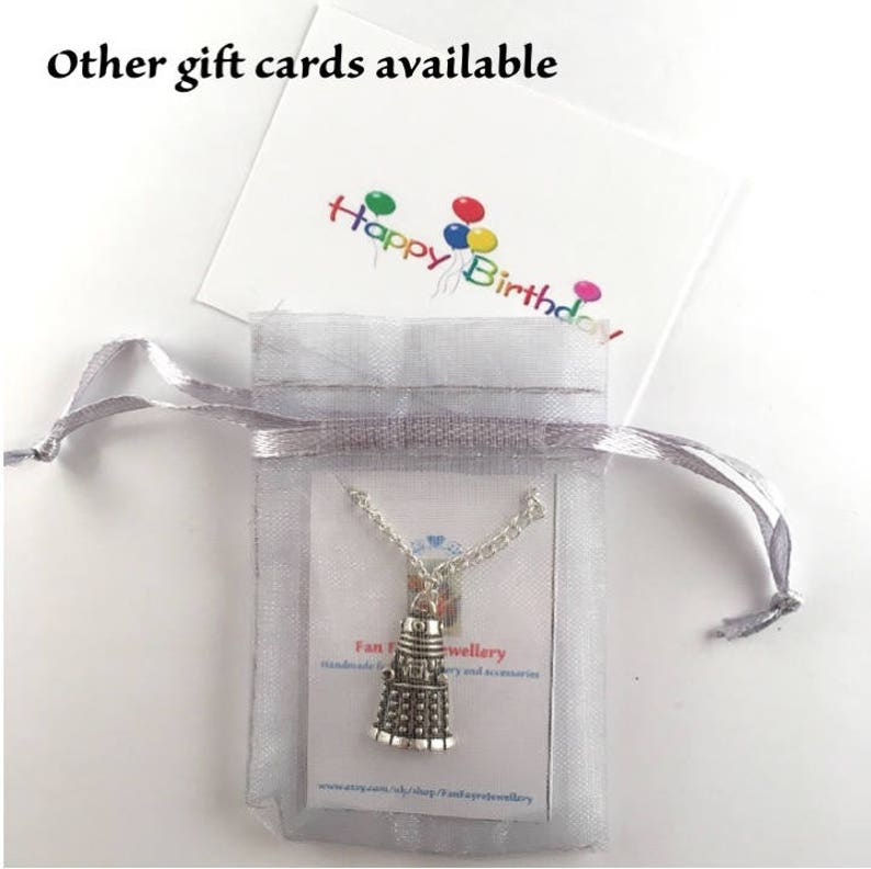 May include: A silver necklace with a charm of a Dalek, a fictional robot from the British science fiction television series Doctor Who. The necklace is packaged in a white organza bag with a card that reads "Fan Jewellery Handmade jewellery and accessories www.etsy.com/uk/shop/FanJewellery".