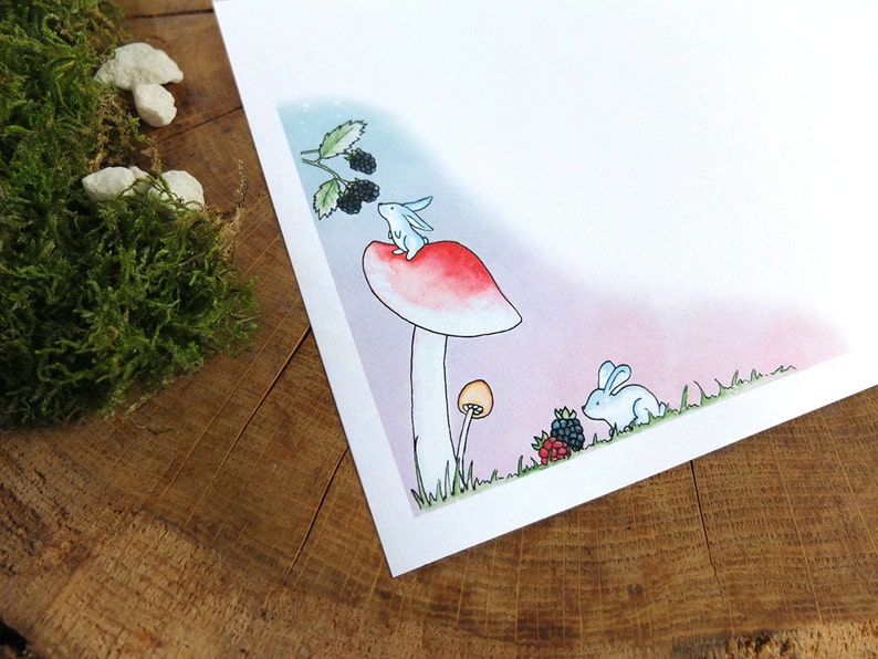 May include: A watercolor illustration of a white rabbit sitting on top of a red and white mushroom with a green stem. There are blackberries on a branch above the rabbit and another white rabbit in the grass below the mushroom.