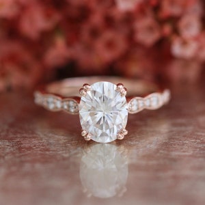 May include: A rose gold engagement ring featuring a large oval-shaped diamond and a delicate band of smaller diamonds.