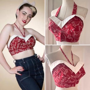 May include: Red halter top with a white trim and a sailboat pattern. The top is a cropped style with a sweetheart neckline. The halter straps and neckline are white. The fabric has a repeating pattern of white sailboats on a red background.