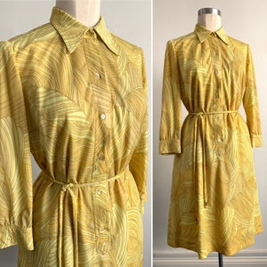 Puede incluir: Un vestido amarillo y amarillo claro con cuello de camisa de manga larga y cinturón de lazo. El vestido tiene un patrón ondulado.