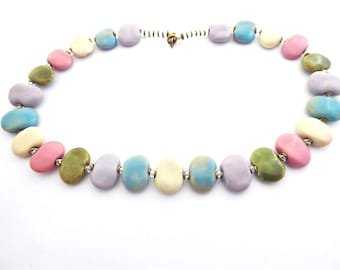 May include: A pastel-colored necklace made of ceramic beads. The beads are shaped like pebbles and are in shades of pink, blue, green, and cream.
