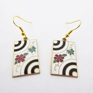May include: A pair of gold tone earrings with white enamel and black geometric designs. The earrings feature pink and blue enamel flowers and butterflies.