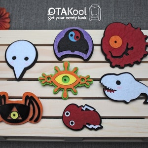 Könnte beinhalten: Sieben Filzpatches mit verschiedenen Anime-Charakteren. Die Patches sind in verschiedenen Farben, darunter Rot, Orange, Gelb, Grün, Blau, Lila und Weiß. Die Patches sind in zwei Reihen auf einer Holzoberfläche angeordnet. Der Text "OTAkool get your nerdy look" ist oben im Bild sichtbar.