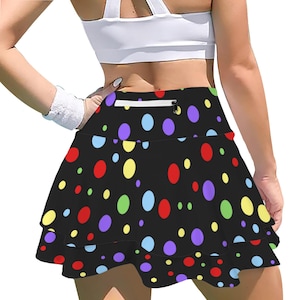 May include: Black athletic skirt with a tiered ruffle design, featuring a colorful polka dot pattern in red, yellow, green, blue, and purple. The skirt has a white zipper pocket and a white waistband.