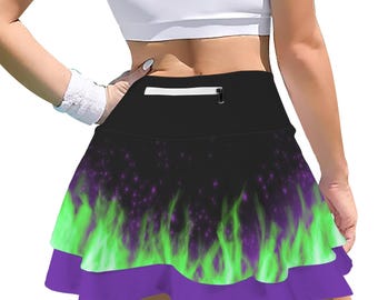May include: A black athletic skirt featuring a vibrant green flame pattern with purple accents and a solid purple bottom ruffle. The skirt includes a high waistband with a horizontal zippered pocket centered on the back for storage.